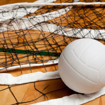A white volleyball on the floor in a darkened gym.See my